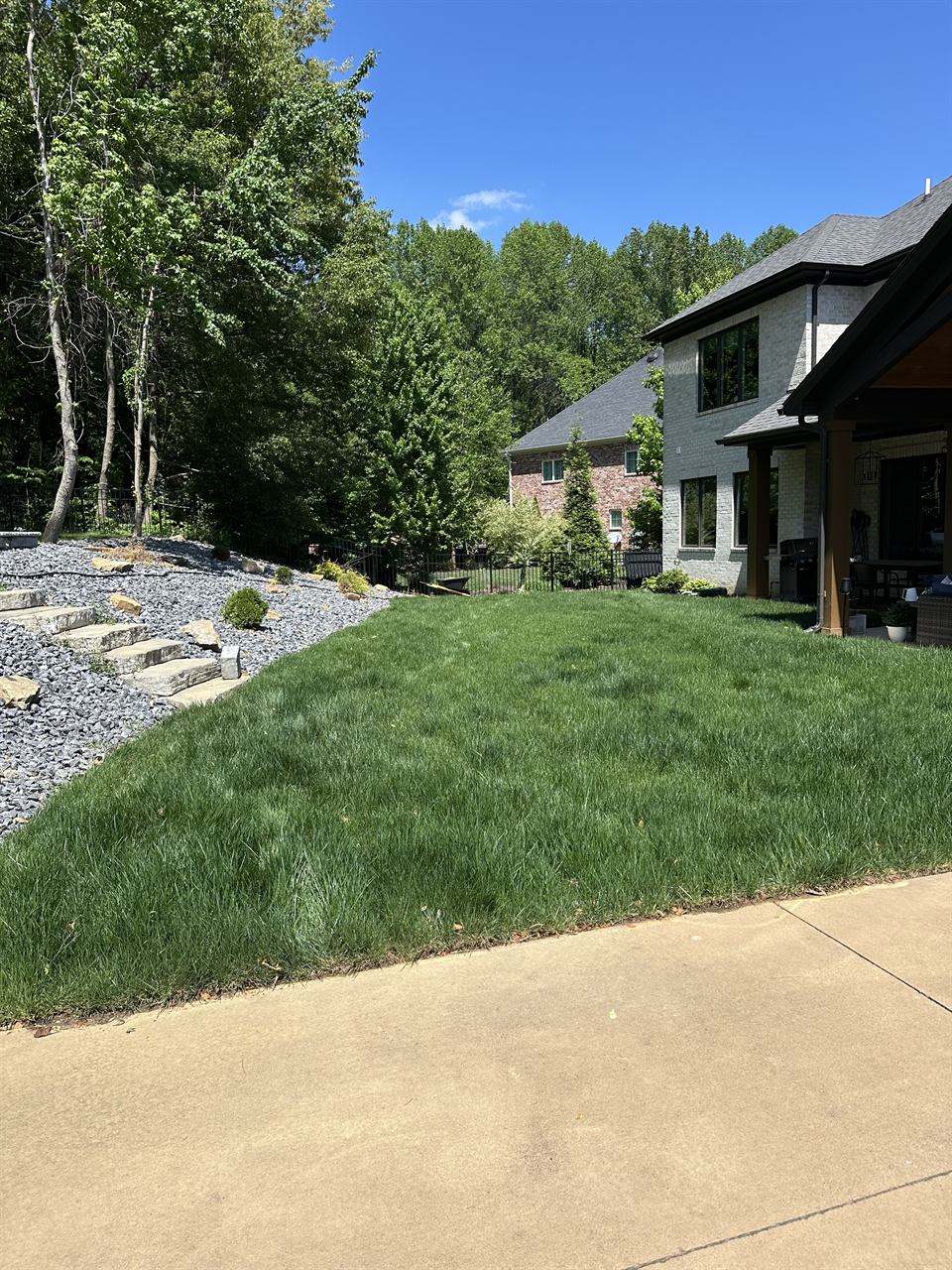 A freshly designed Owensboro landscape with a manicured lawn, stone border, and layered plantings beside a modern home