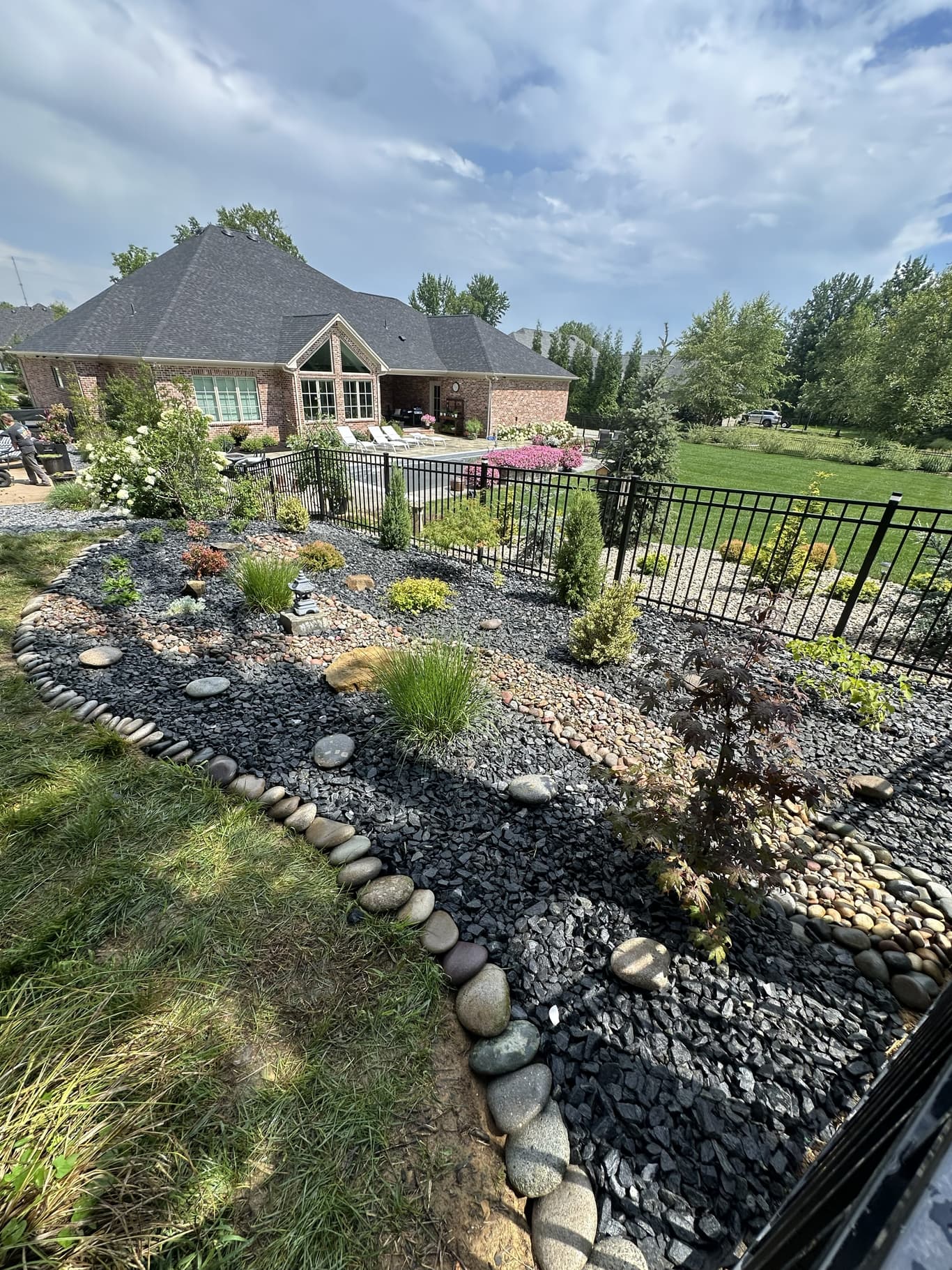 A completed Horizon Outdoor Solutions hardscape project in Owensboro, KY with a decorative stone bed, dry creek drainage, river rock borders, and layered plantings beside a brick home